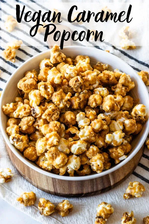 a white bowl filled with caramel popcorn on top of a striped cloth next to a wooden spoon