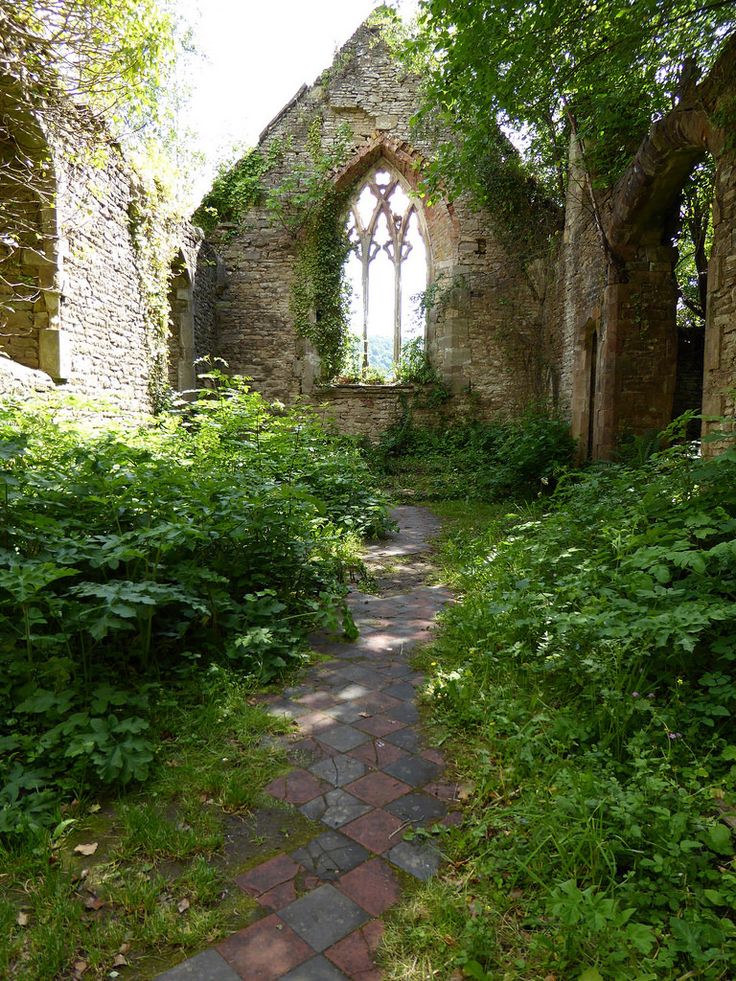 an old stone building with a large window in it's center surrounded by greenery