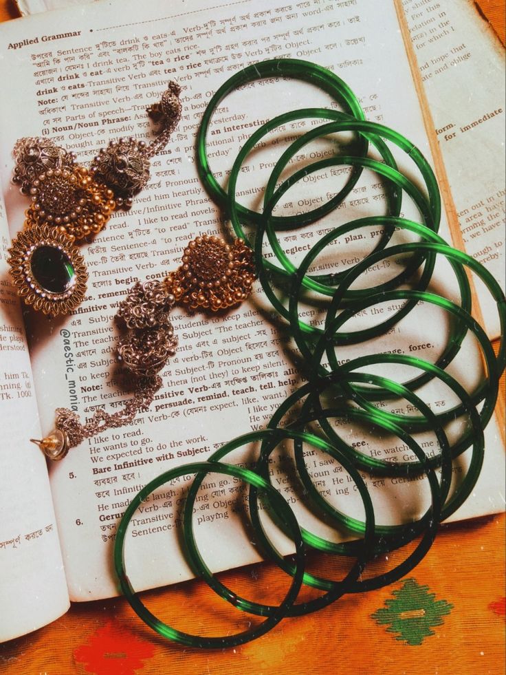 several green bracelets are laying on top of an open book and some other jewelry