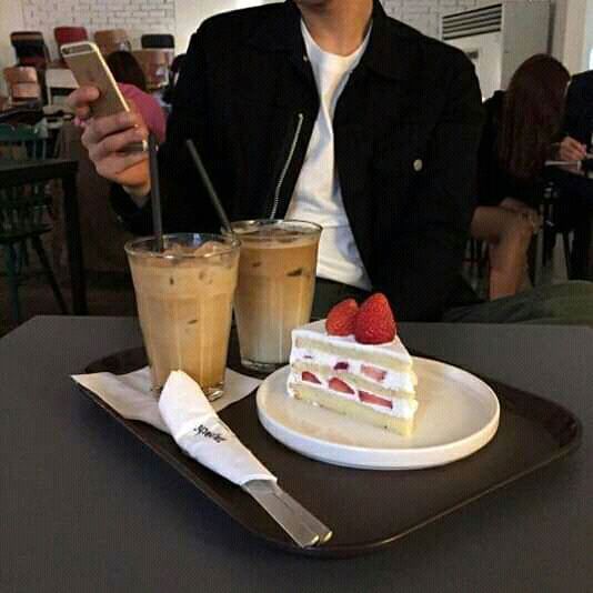 a man sitting at a table with two drinks and a piece of cake on the plate