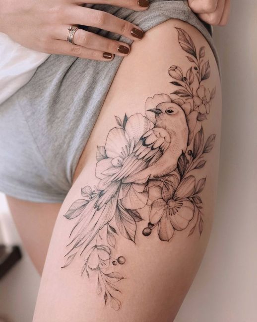 a woman's thigh with flowers and a bird tattoo on her leg, while she is wearing grey shorts