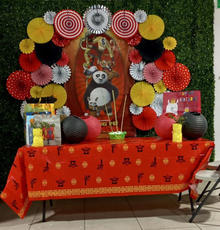 a table topped with red and yellow paper fans next to a wall covered in greenery