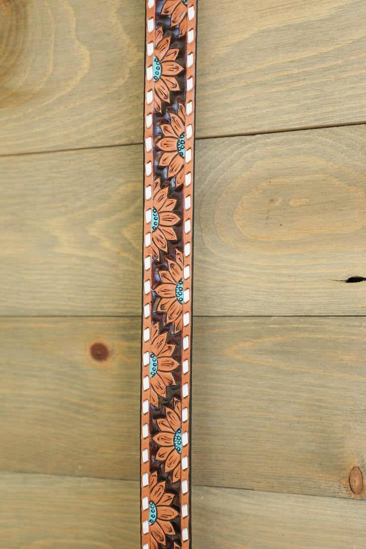 a brown and blue flowered belt on wooden planks next to a wall with wood boards in the background