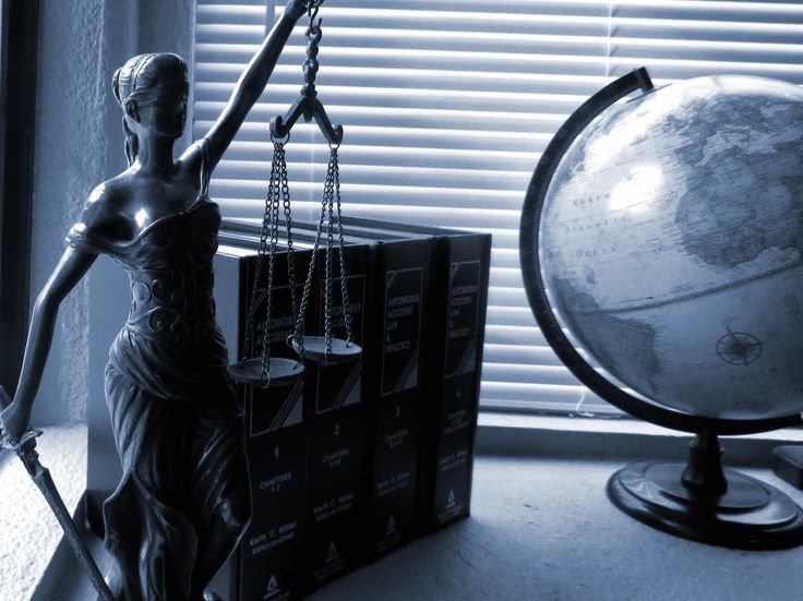 a statue of lady justice standing next to a globe on a table in front of a window