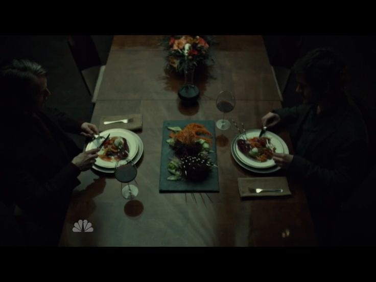 two people sitting at a table with plates of food in front of them and flowers on the table