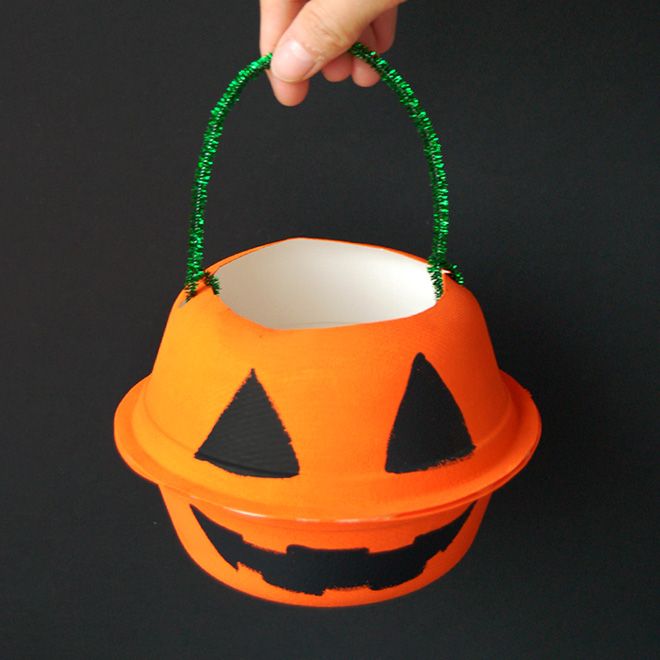 a hand holding an orange bucket with a jack o lantern on it