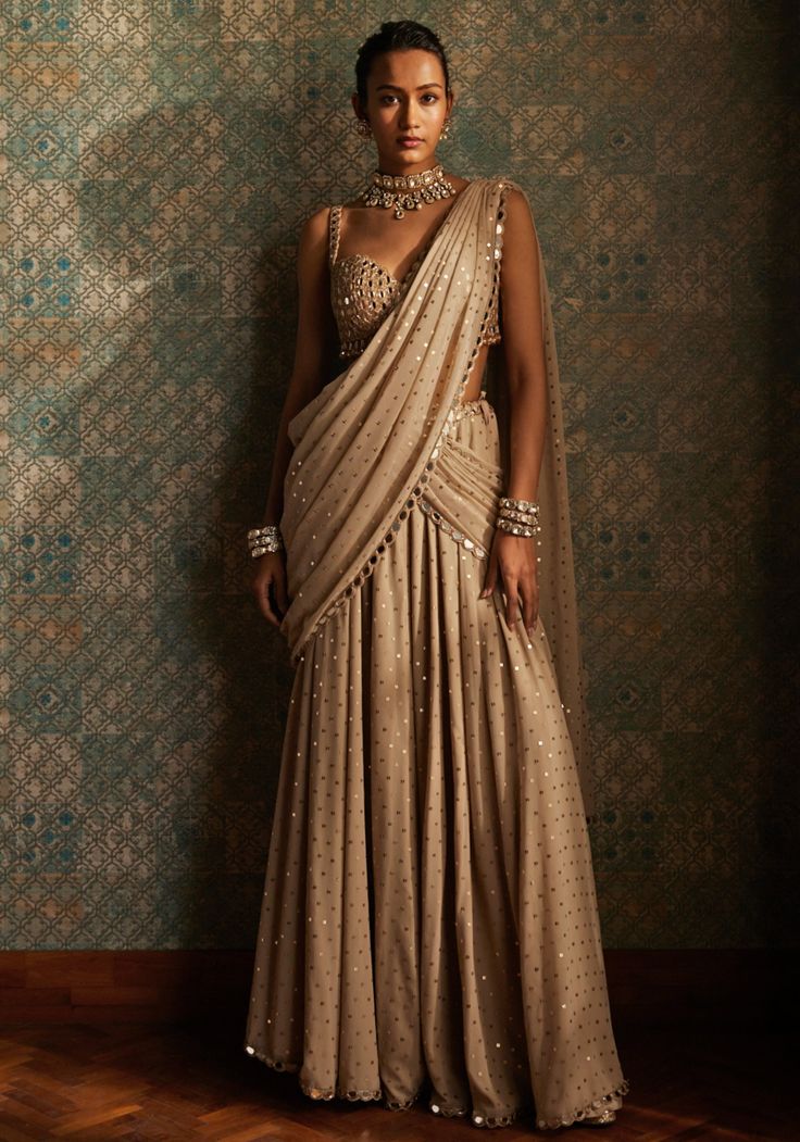 Elevate your style with our exquisite beige gold pre-draped saree and mirror blouse set. Crafted from luxurious beige georgette fabric, this saree features intricate sequins work and is completed with a mirror work border, enhanced with rose gold embroidery. Teamed with a hand cut mirrorwork sleeveless blouse that adds a touch of elegance to the ensemble. With its pre-draped design, this saree is perfect for those who want to effortlessly look glamorous. Embrace the beauty of this saree and make Contemporary Lehenga, Mirror Work Border, Mirror Lehenga, Pre Draped Saree, Mirror Blouse, Contemporary Saree, Vani Vats, Cotton Sarees Handloom, Embroidery Mirror