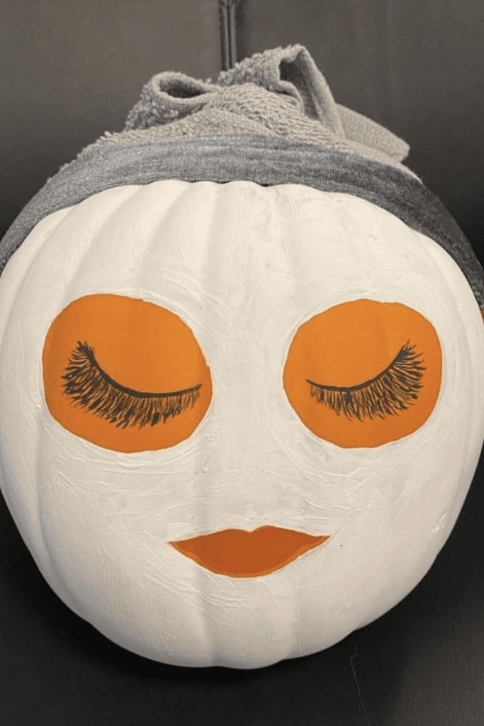 a white pumpkin with orange eyes and lashes painted on it's face, sitting on a black surface