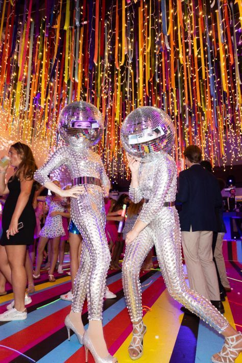 two people in disco costumes dancing on a colorful floor