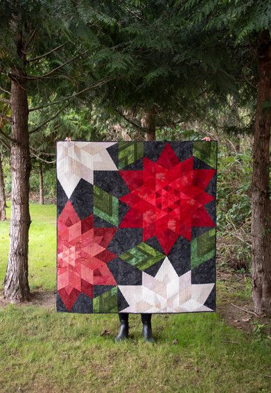 a woman standing in the grass with a quilt on her chest and red poinsettia