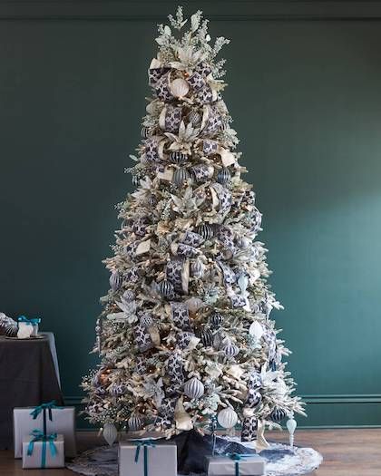 a white christmas tree with blue and silver ornaments on it's branches, surrounded by presents