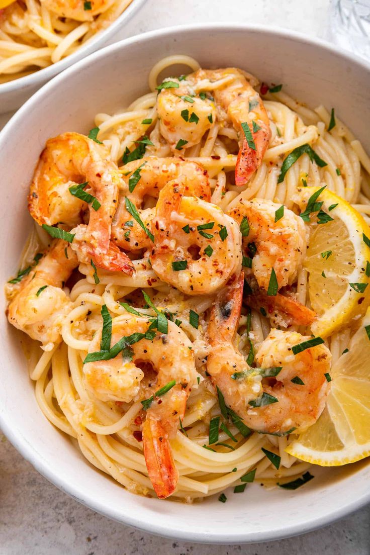 two bowls filled with pasta and shrimp, garnished with parsley on the side