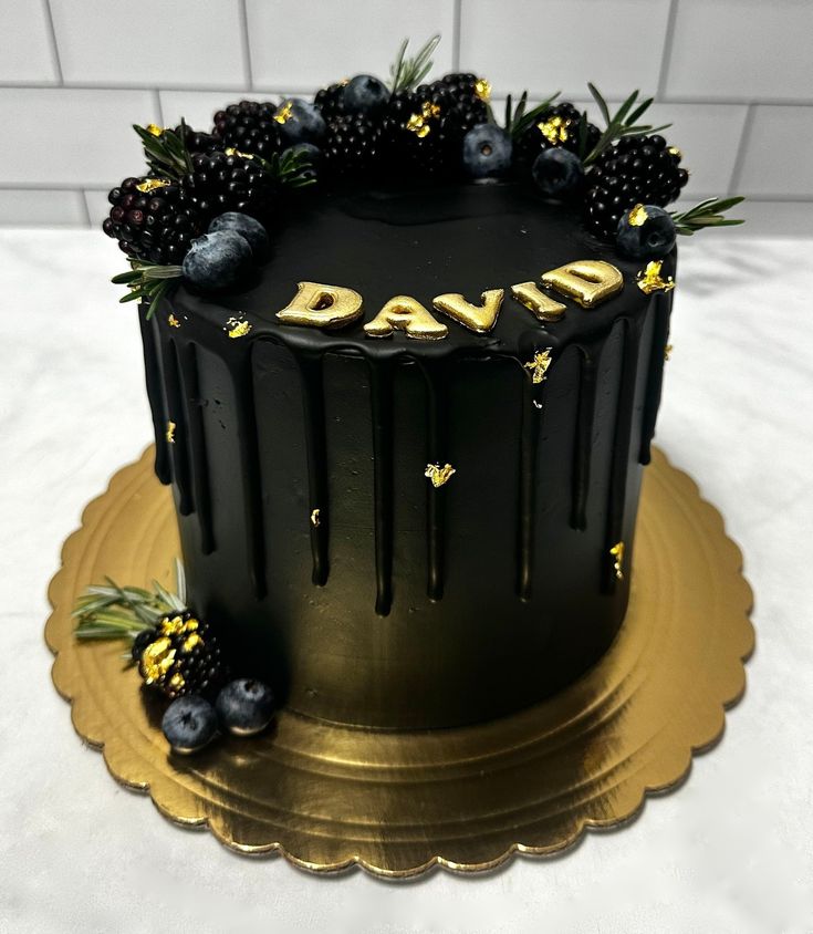 a black cake with gold lettering and berries on top is sitting on a golden plate