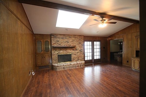 an empty living room with hard wood flooring and a brick fireplace in the center