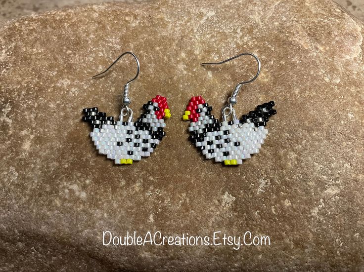 a pair of chicken earrings made out of seed beads on top of a large rock