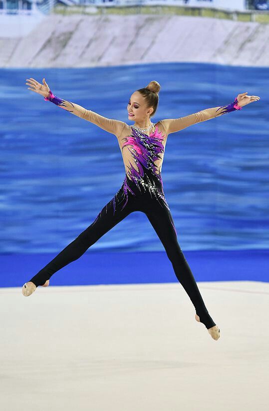 a woman is doing a trick on the ice in front of some water and buildings