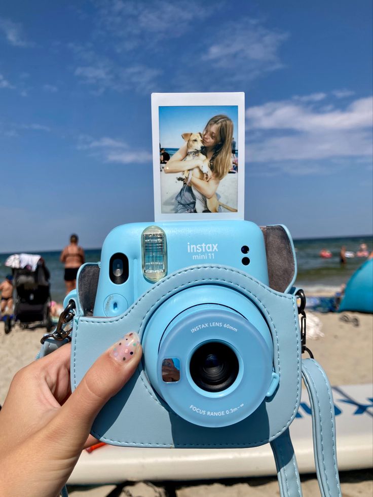 a person holding up a camera with a dog on the beach in the back ground