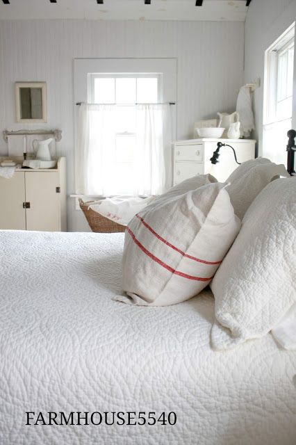 a bed with white linens and pillows in a bedroom next to a window,