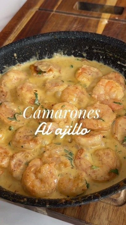 a skillet filled with shrimp and sauce on top of a wooden cutting board