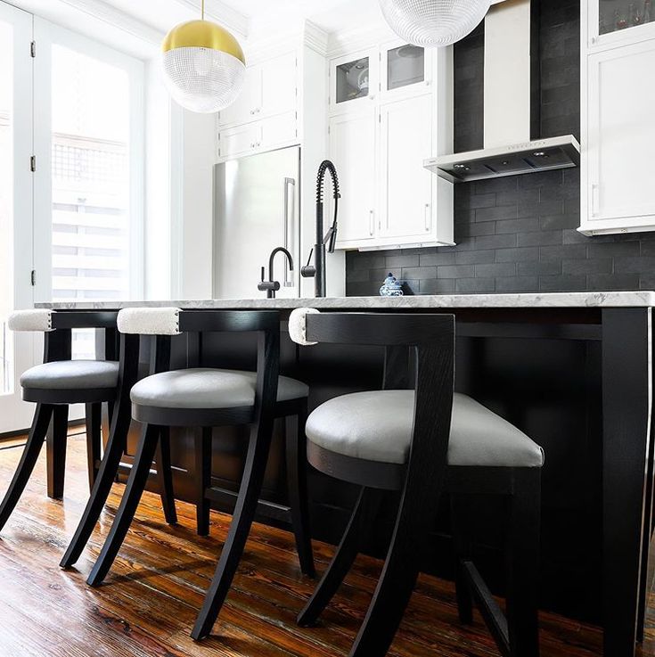 a kitchen with white cabinets and black countertops, stools at the center island