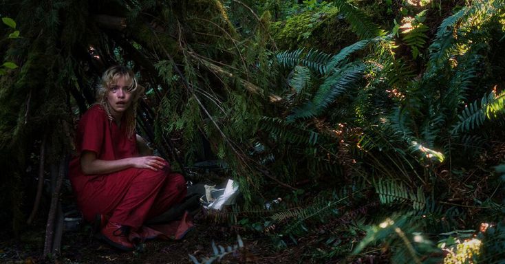 a woman in a red dress sitting on the ground surrounded by plants and trees,