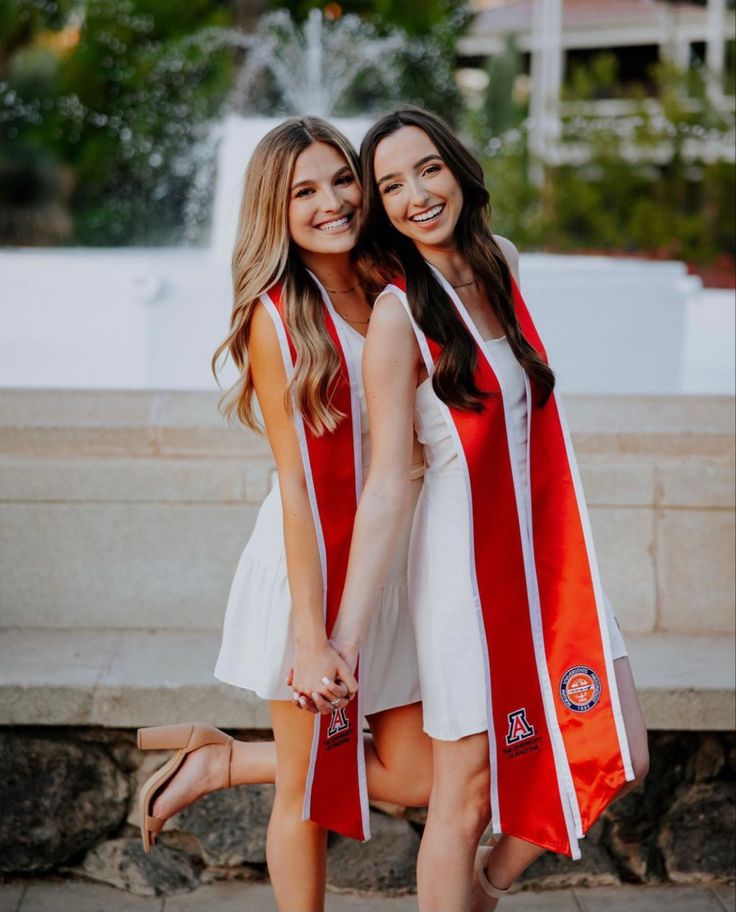 two young women in graduation gowns holding hands