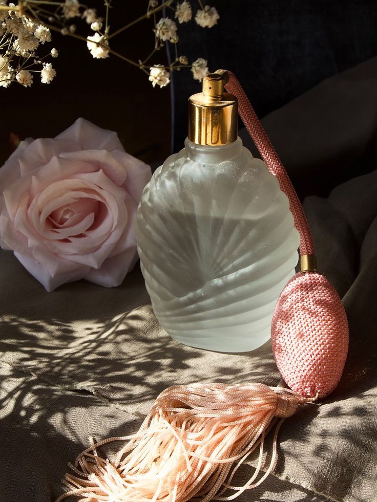 a white bottle sitting on top of a bed next to a pink rose and a flower