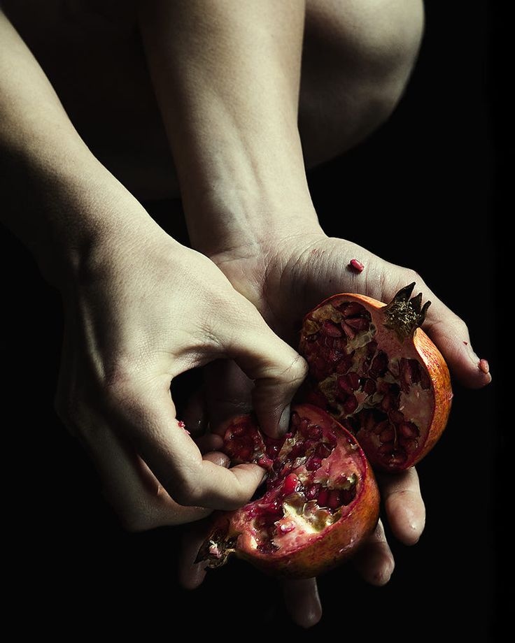 a person holding a half eaten pomegranate in their hands, on a black background