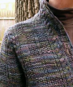 a close up of a person wearing a sweater next to a tree