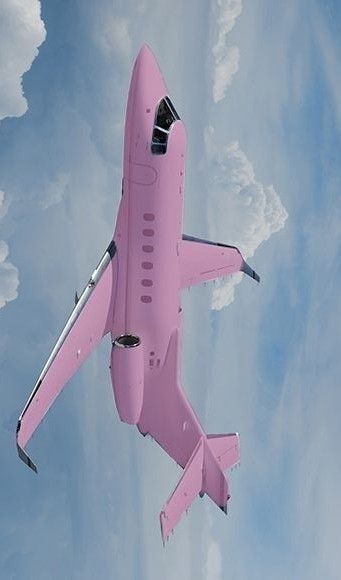 a pink airplane flying in the sky with clouds