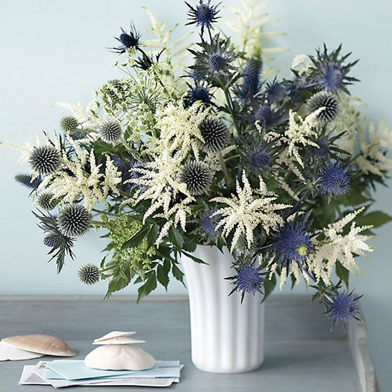 a white vase filled with blue and white flowers next to a seashell on a table