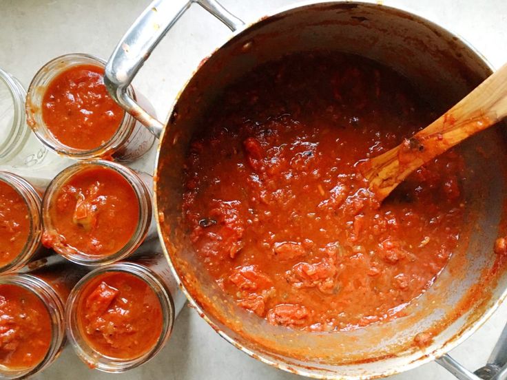 a pot filled with sauce next to small jars