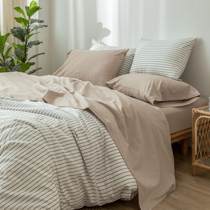 an unmade bed with two pillows on top of it and a plant in the corner