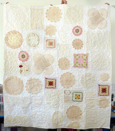 a woman holding up a large quilt with many different designs on it