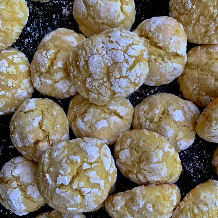 a pile of powdered sugar cookies sitting on top of a black countertop next to other pastries