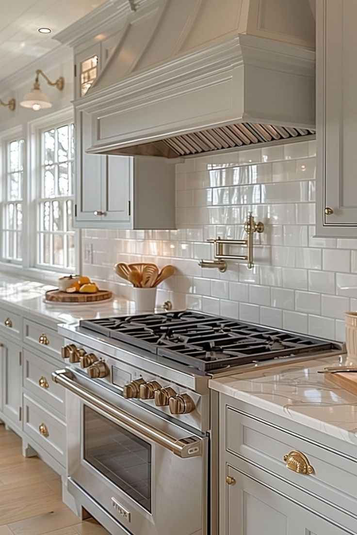 a kitchen with white cabinets and gold trim on the stove top, along with an oven hood