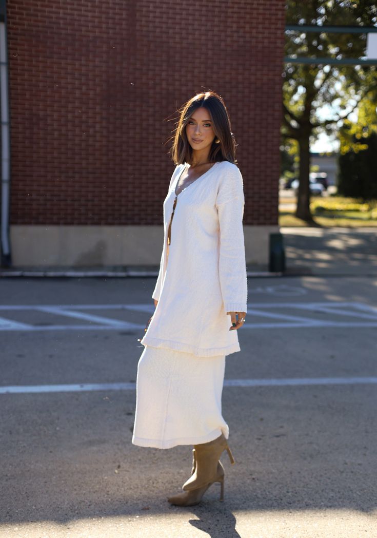 a woman is standing in the street wearing a white coat and boots with her hands in her pockets