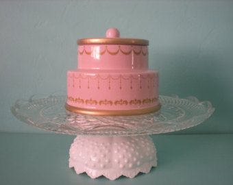 a pink cake sitting on top of a glass platter with a gold trimming