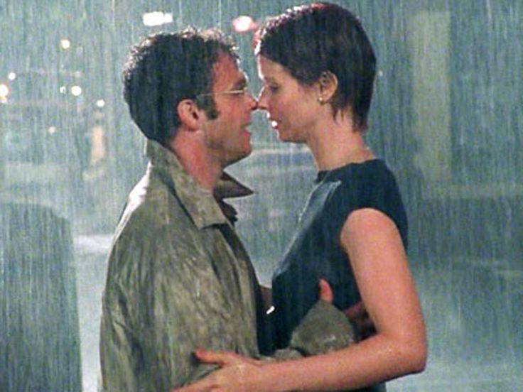 a man and woman standing in the rain with their arms around each other as they look into each others eyes