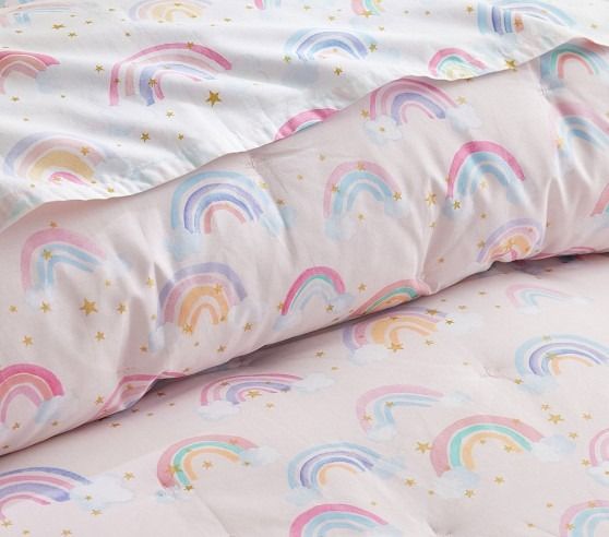 a pink bed with rainbows and stars on the comforter is next to a pillow