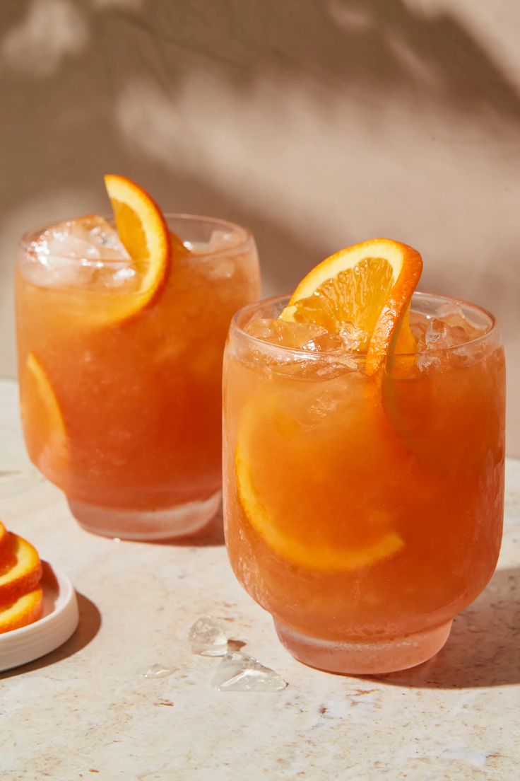 two glasses filled with orange juice and garnished with an orange slice on the rim