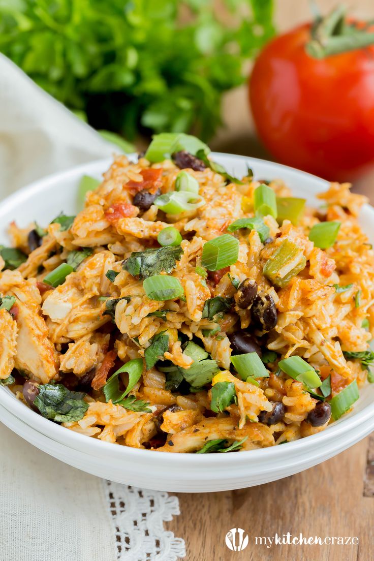 a white bowl filled with mexican rice and beans next to a red tomato on the side