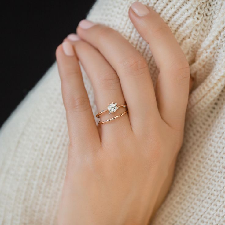 a woman's hand wearing a gold ring with a small diamond on the middle