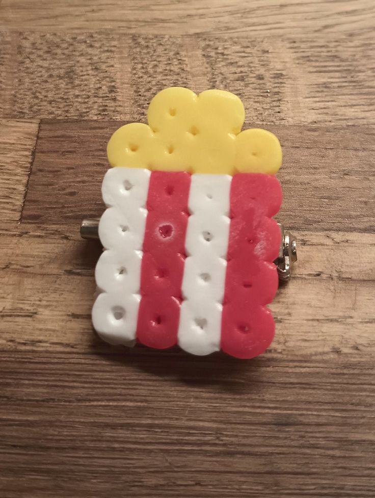 a red, white and yellow brooch sitting on top of a wooden table