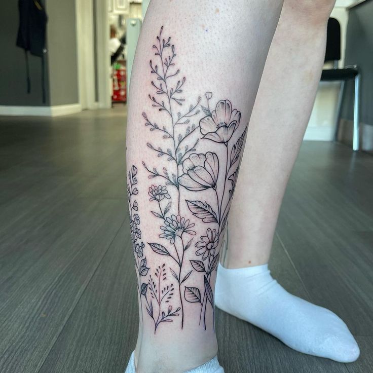 #flowers #legwraptattoo #fineline #wildflowertattoo #calvetattoo #longstems #hand-drawn #femininetattoo #beautifultattoo Floral Tattoo Design Calf, Flowers On Calf Tattoo, Birth Flower Tattoos On Leg, Flower Wrap Ankle Tattoo, Botanical Leg Wrap Tattoo, Flowers Wrapped Around Ankle Tattoo, Flowers Calf Tattoo, Flower Garden Leg Tattoo, Flower Around Ankle Tattoo