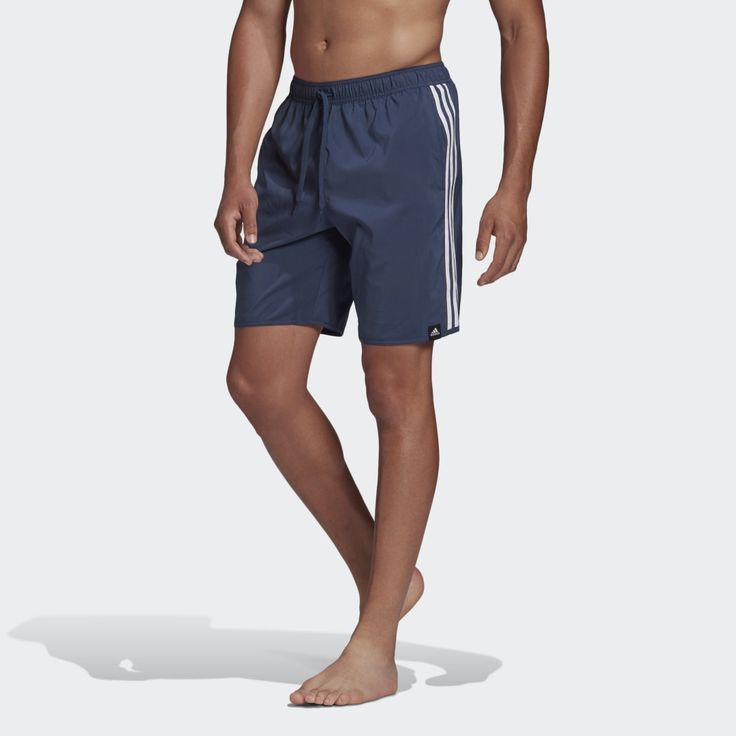 a man standing in front of a white background wearing adidas swim trunks and no shirt