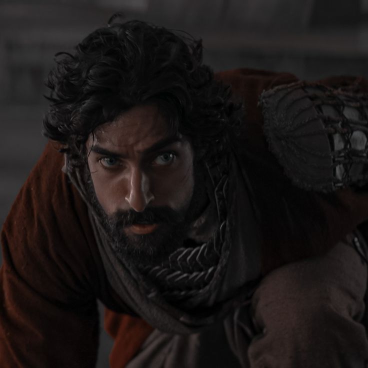 a man with long black hair and beard wearing a red shirt is looking at the camera