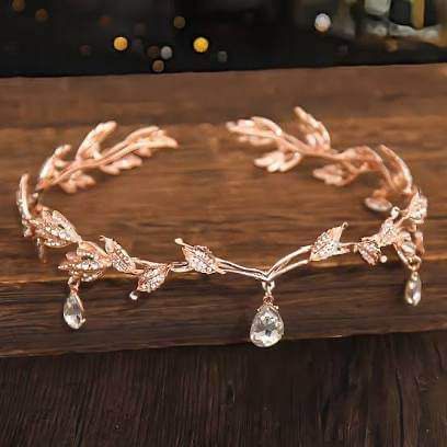 a gold bracelet with leaves and crystal stones on the side, sitting on top of a wooden