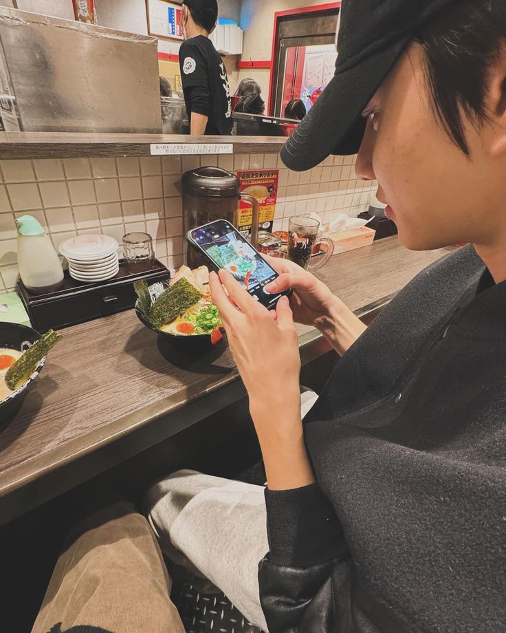 a person sitting at a counter using a cell phone in a kitchen with food on the counter