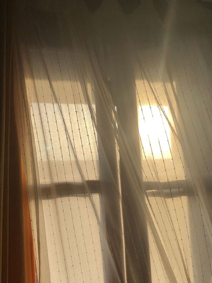 the sun shines through sheer curtains in front of a window